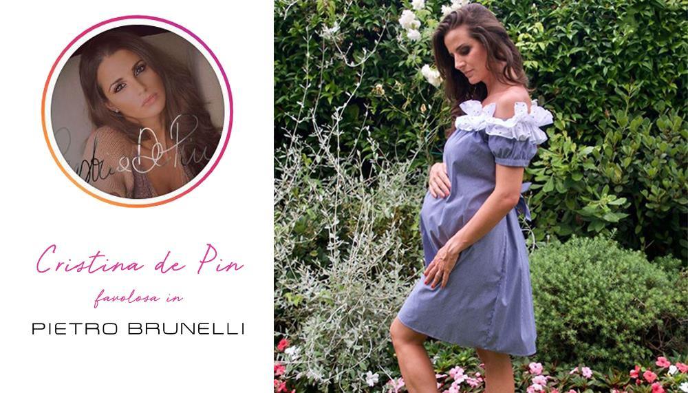 Donna incinta in abito premaman viola con dettagli bianchi in giardino fiorito