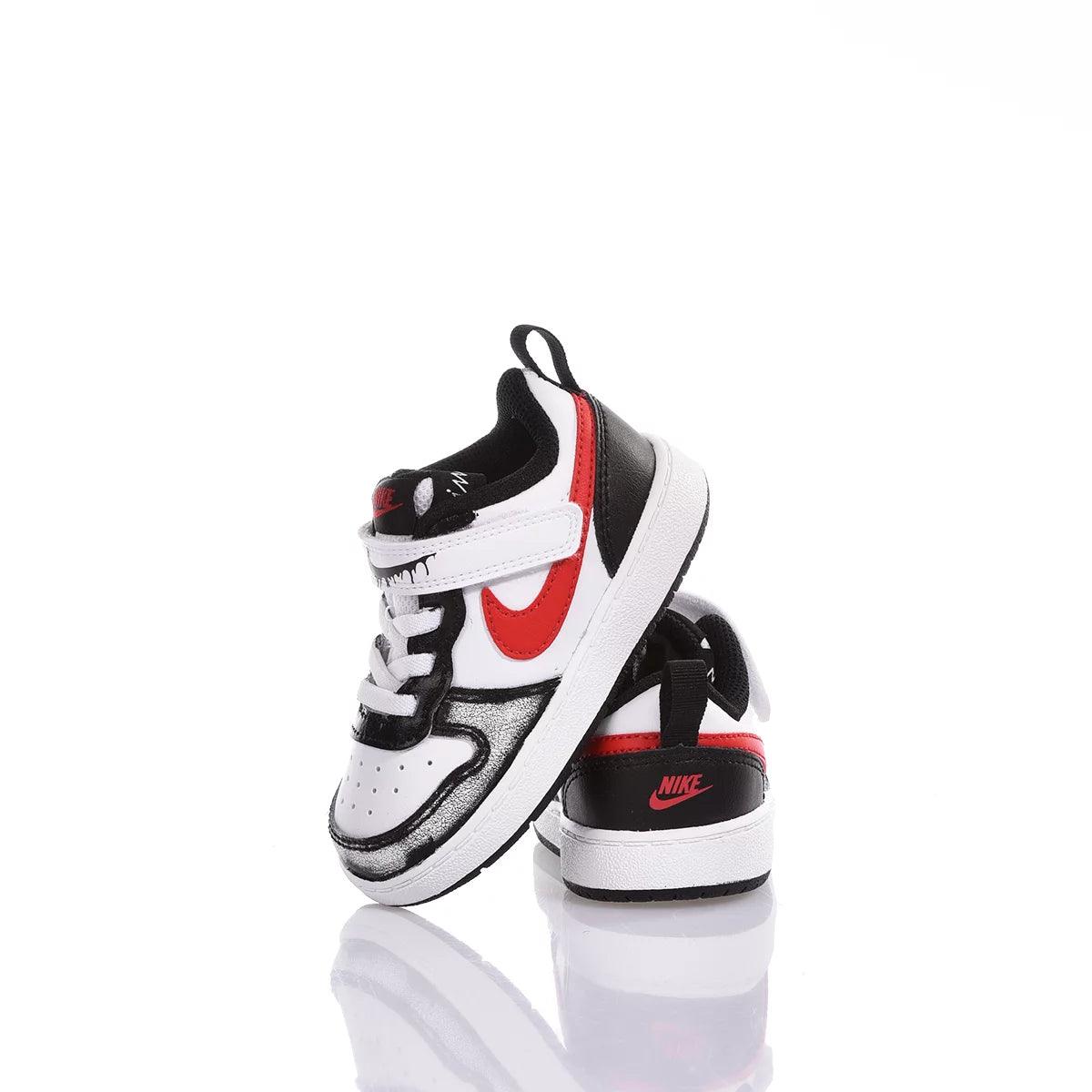 Scarpe sportive bambino bianche e nere con dettagli rossi, su sfondo bianco riflettente.