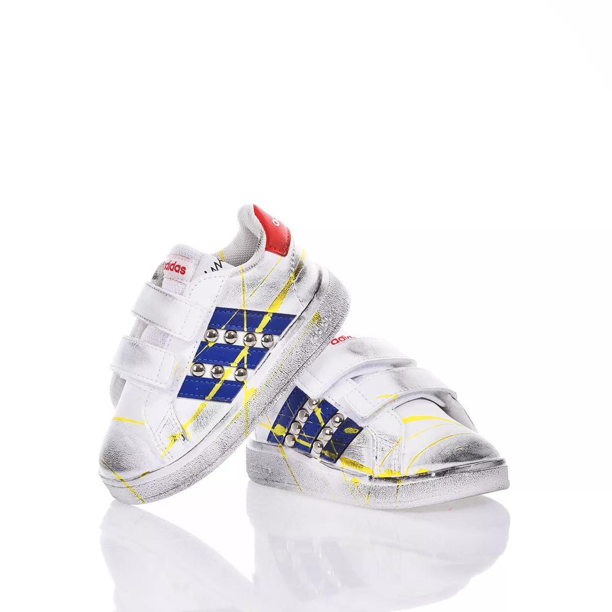 Scarpe sportive bianche da bambino con dettagli blu e gialli, borchie e chiusura a strappo.