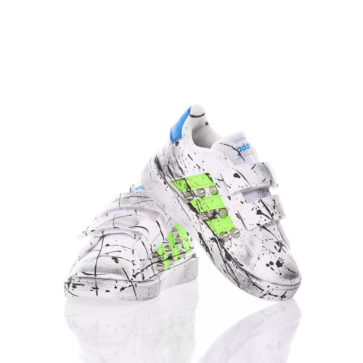 Scarpe sportive bianche con dettagli verdi, borchie e fantasia a schizzi neri, chiusura a strappo.