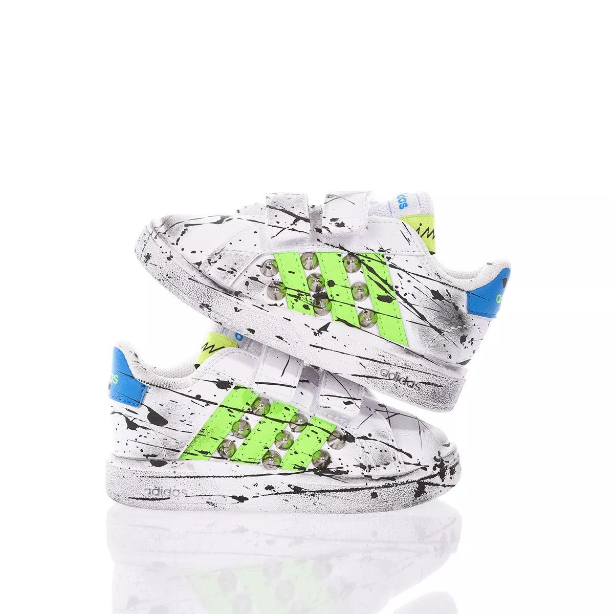 Sneakers bianche per bambini con dettagli verdi e blu, design con schizzi di vernice nera.
