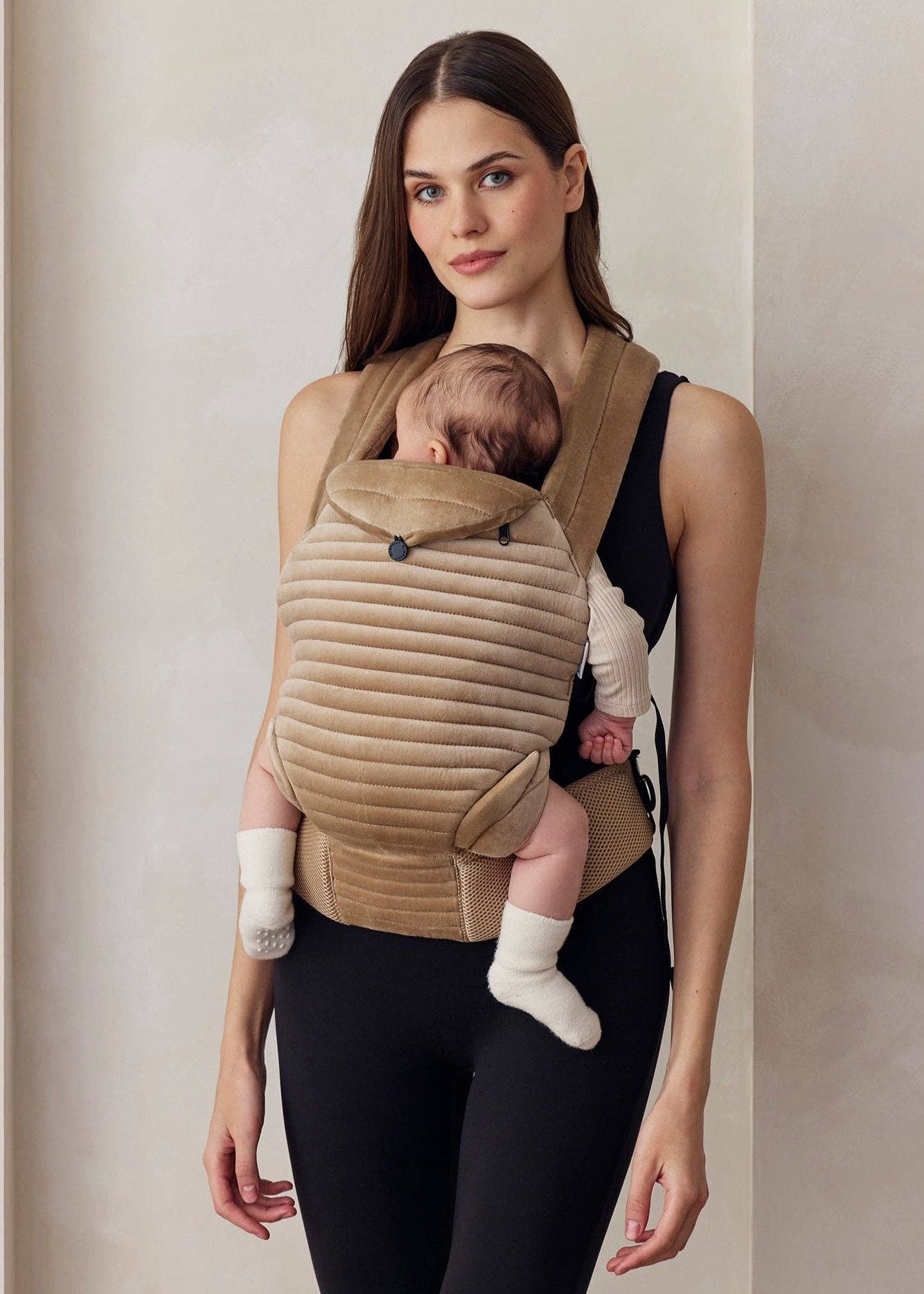 Donna indossa abbigliamento premaman e porta un neonato in marsupio beige imbottito.