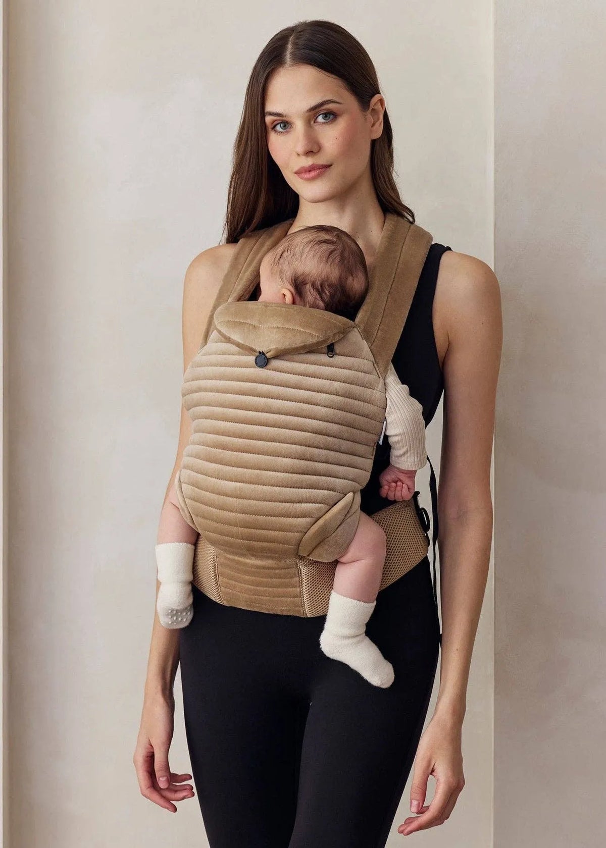 Donna indossa abbigliamento premaman e porta un neonato in marsupio beige imbottito.