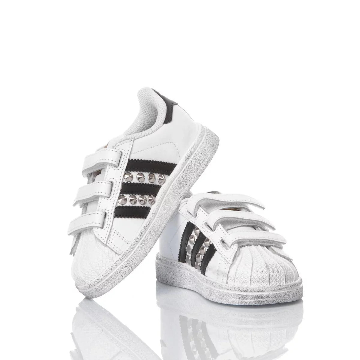 Scarpe da ginnastica bianche per bambini con strisce nere e borchie, chiusura a strappo.