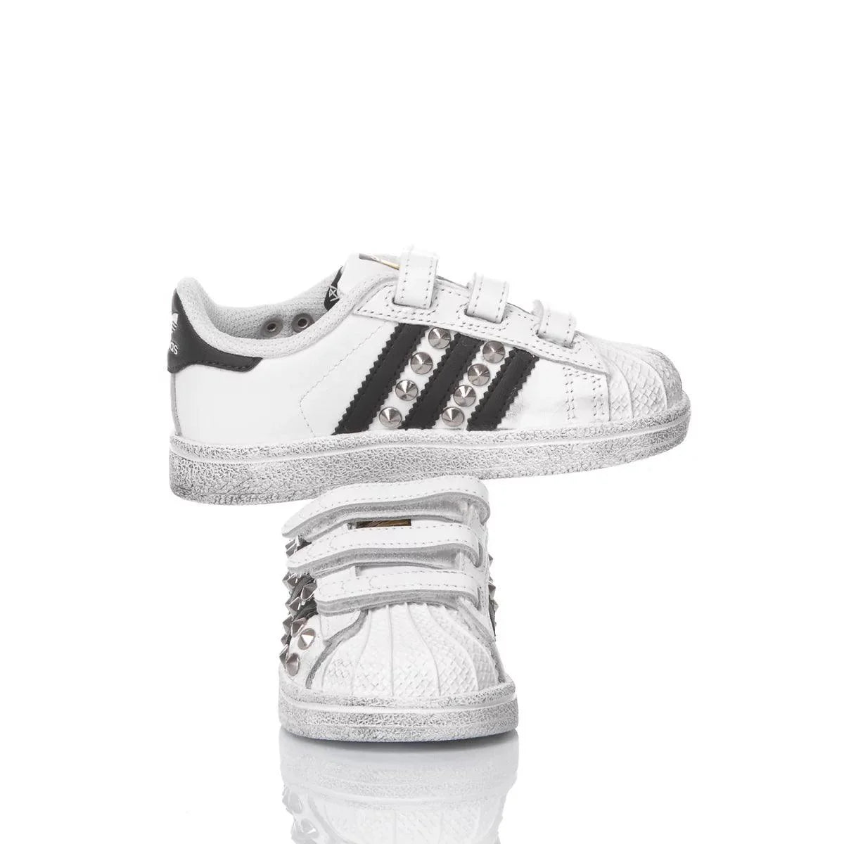 Scarpe da bambino bianche con dettagli neri, borchie e chiusura a strappo in evidenza.