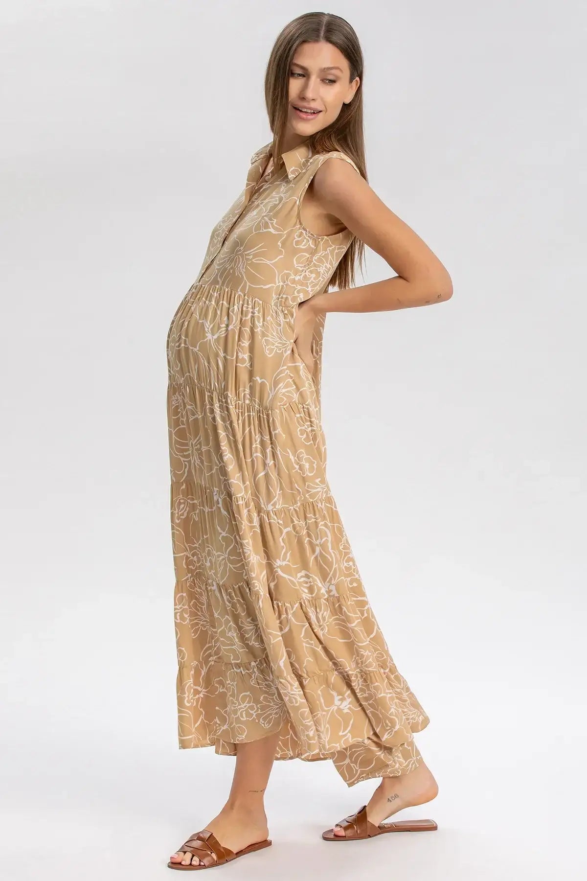 Donna incinta indossa abito premaman lungo beige senza maniche con fantasia floreale bianca