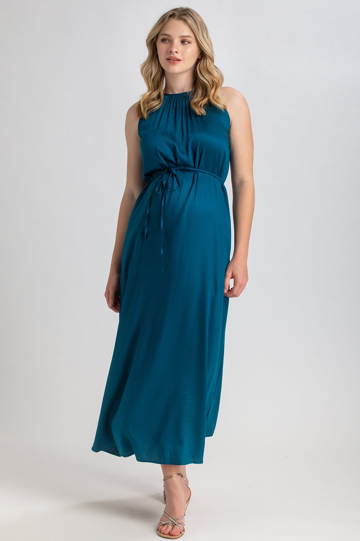 Donna incinta indossa abito premaman lungo senza maniche blu petrolio, vestibilità elegante.