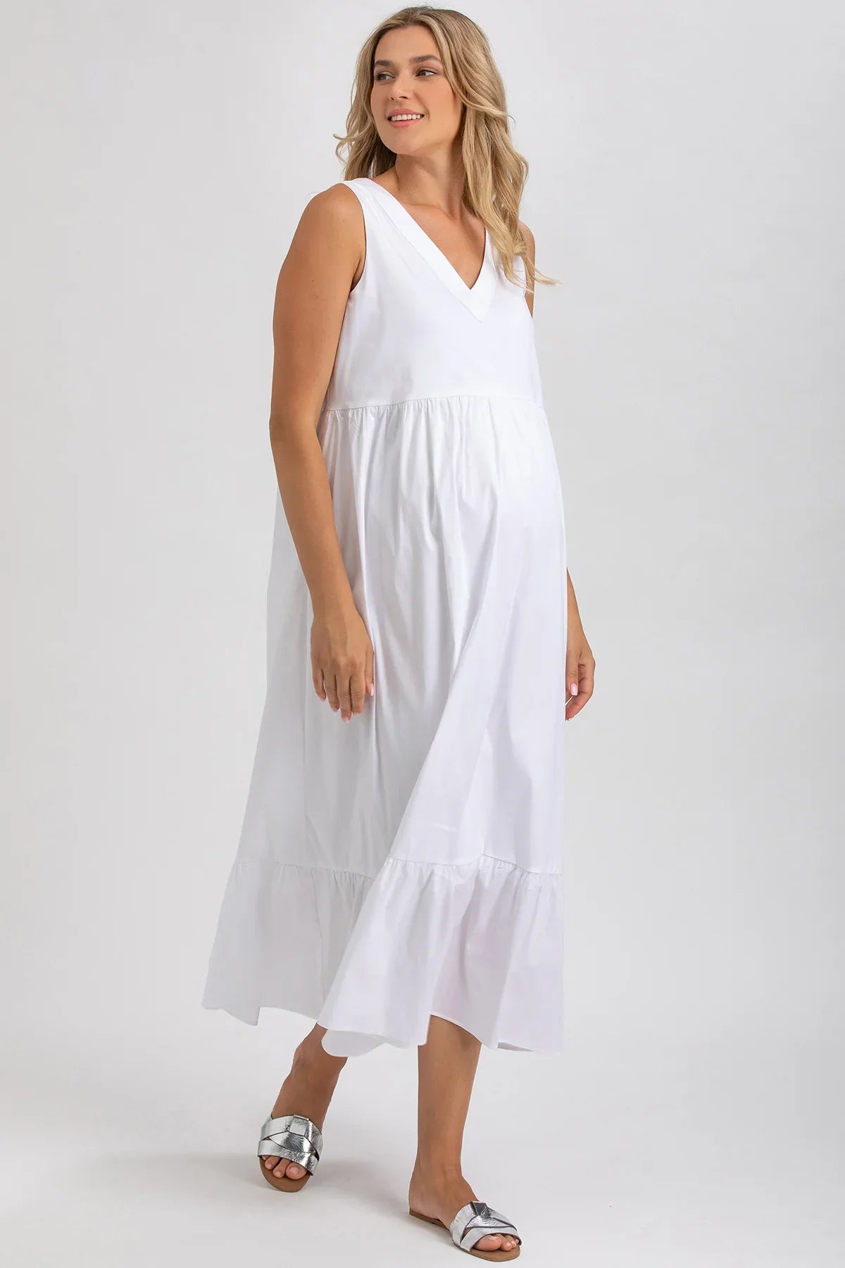 Donna incinta indossa abito premaman bianco senza maniche, stile estivo elegante.