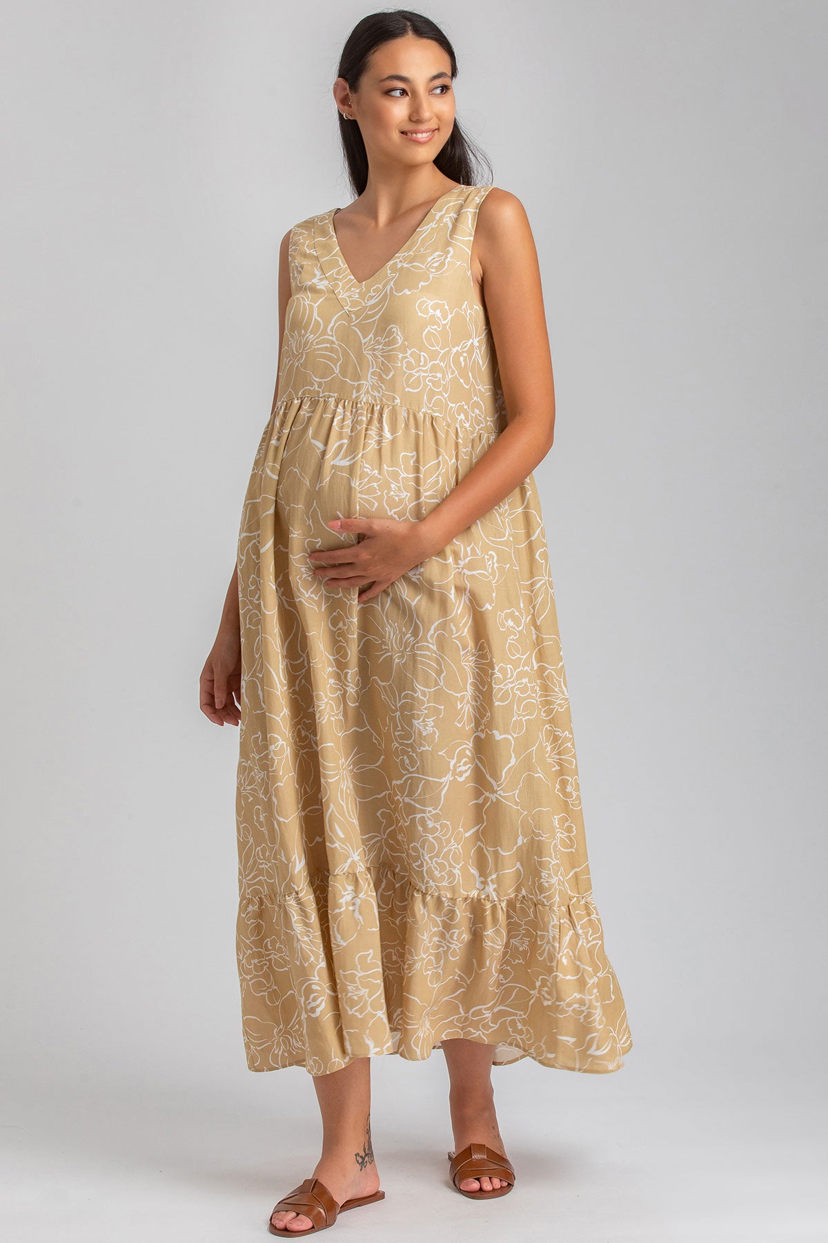 Donna incinta con abito premaman lungo beige a fiori bianchi, senza maniche, su sfondo neutro