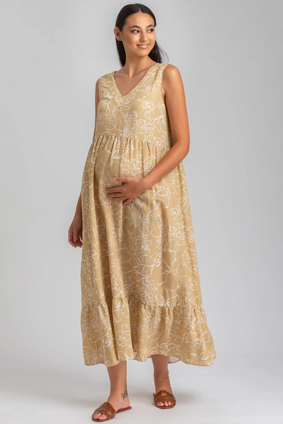 Donna incinta con abito premaman lungo beige a fiori bianchi, senza maniche, su sfondo neutro