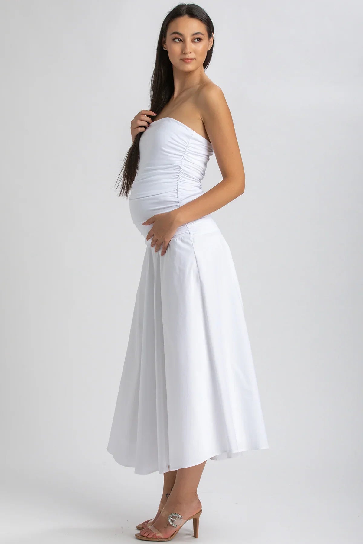 Donna incinta con abito premaman bianco senza spalline, elegante e fluido