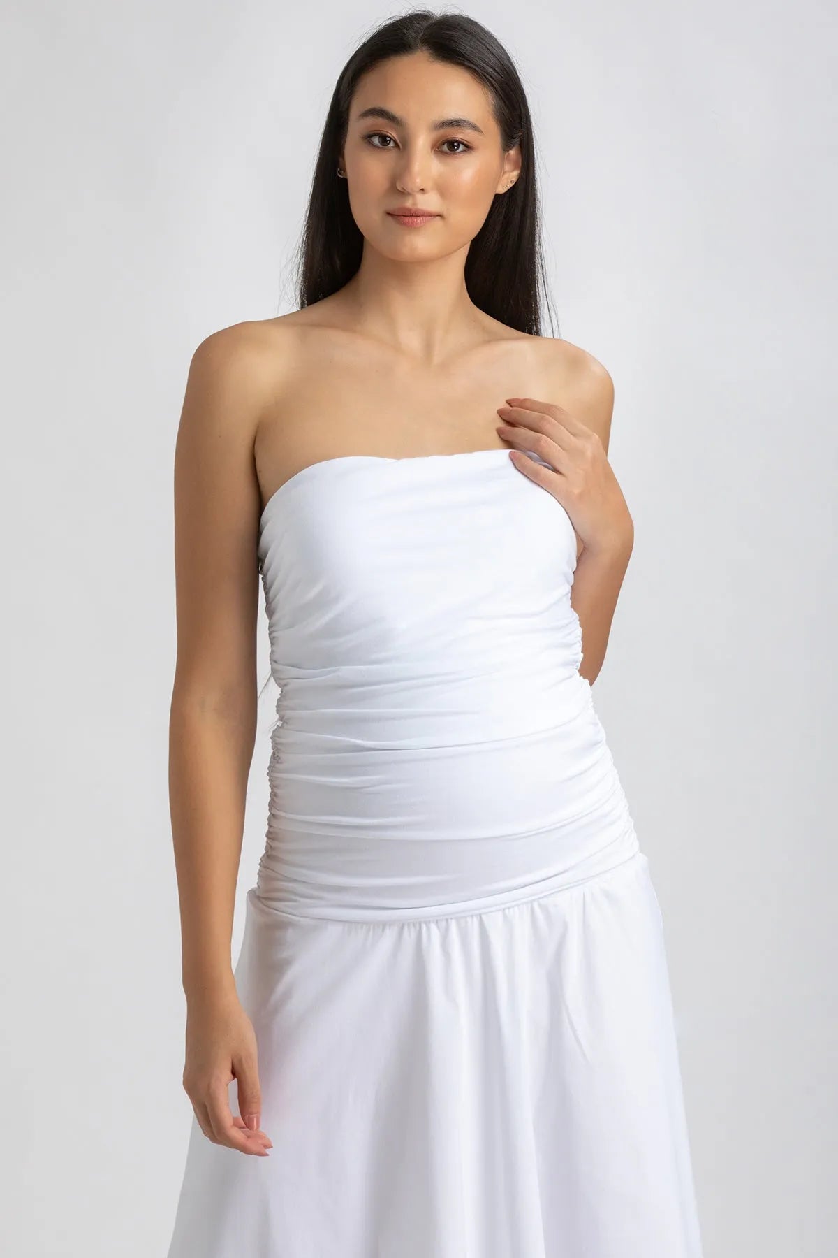 Donna con abito premaman bianco senza spalline, tessuto arricciato e gonna ampia.