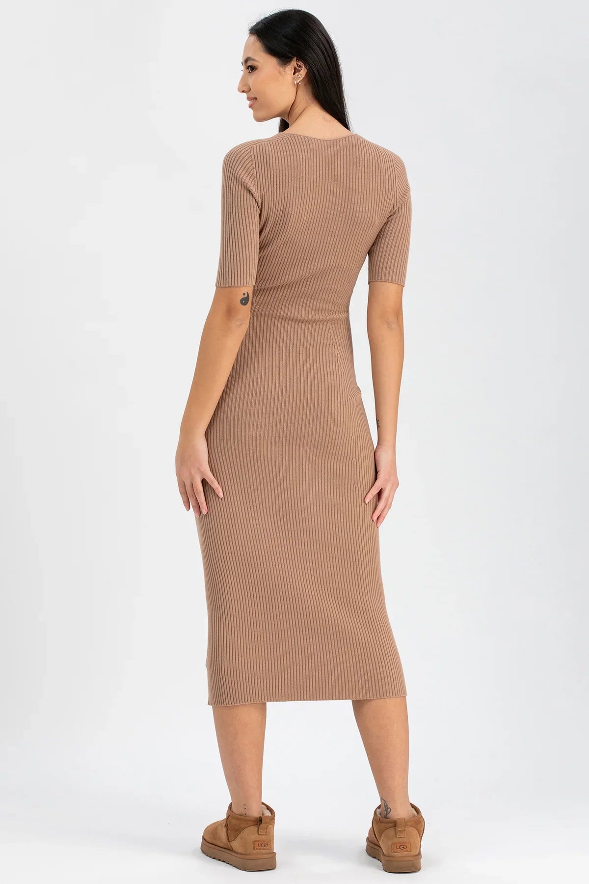 Donna di profilo con abito premaman beige a costine, maniche corte, su sfondo chiaro.