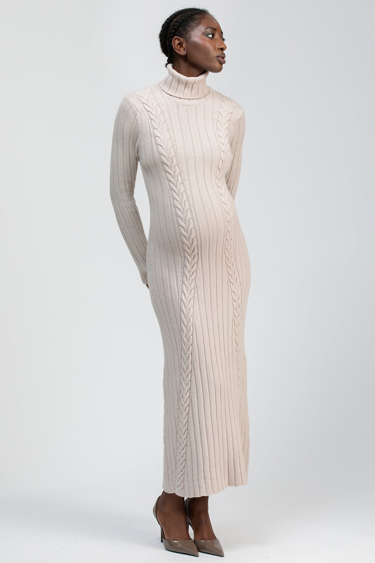 Abito premaman lungo a collo alto in maglia beige con lavorazione a trecce, donna in posa elegante.