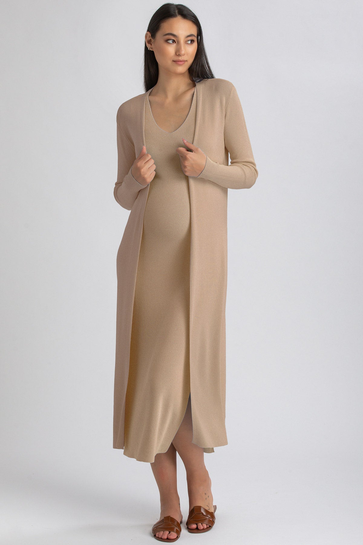 Modella indossa abito premaman lungo beige in maglia a maniche lunghe, su sfondo neutro