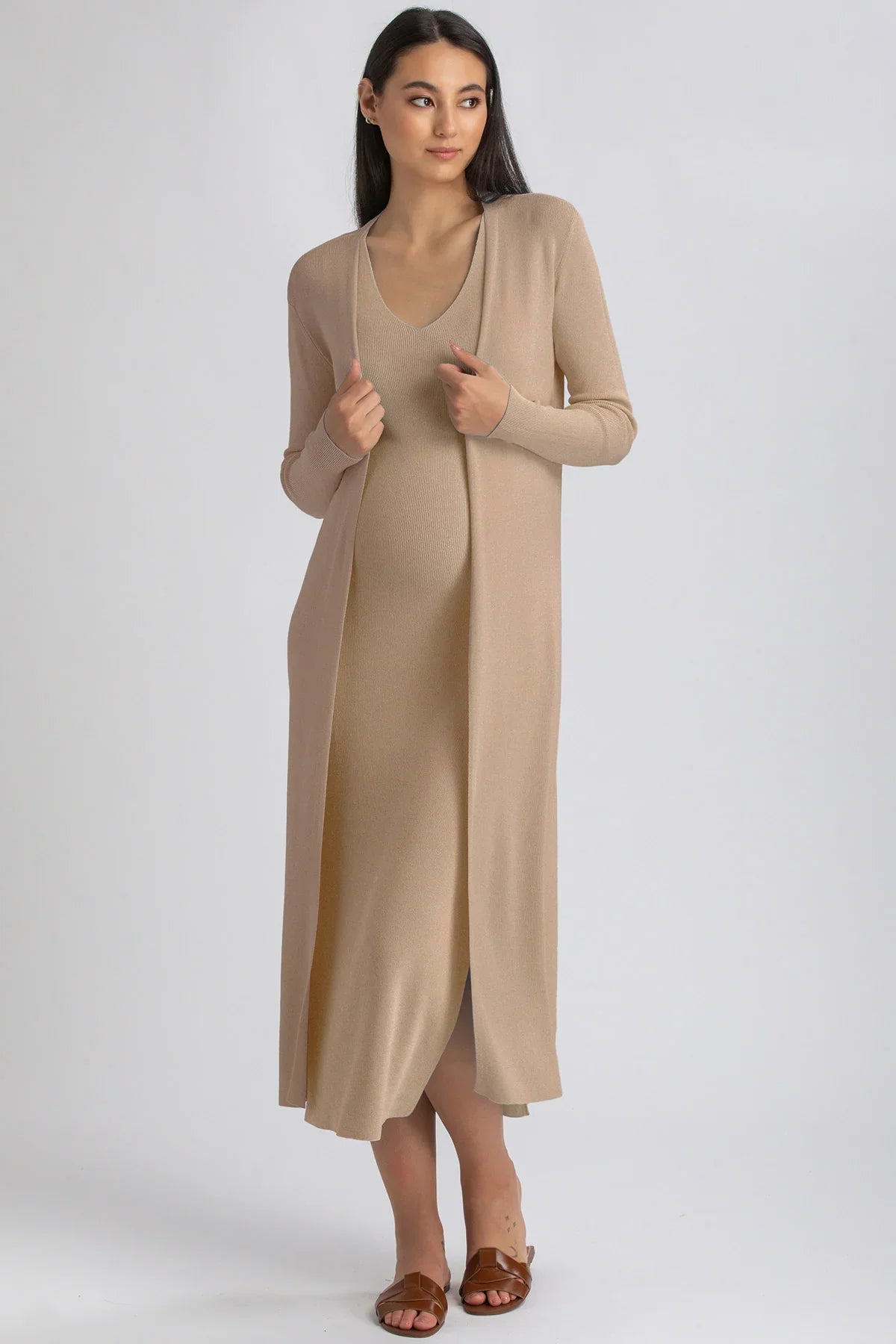 Modella indossa abito premaman lungo beige in maglia a maniche lunghe, su sfondo neutro