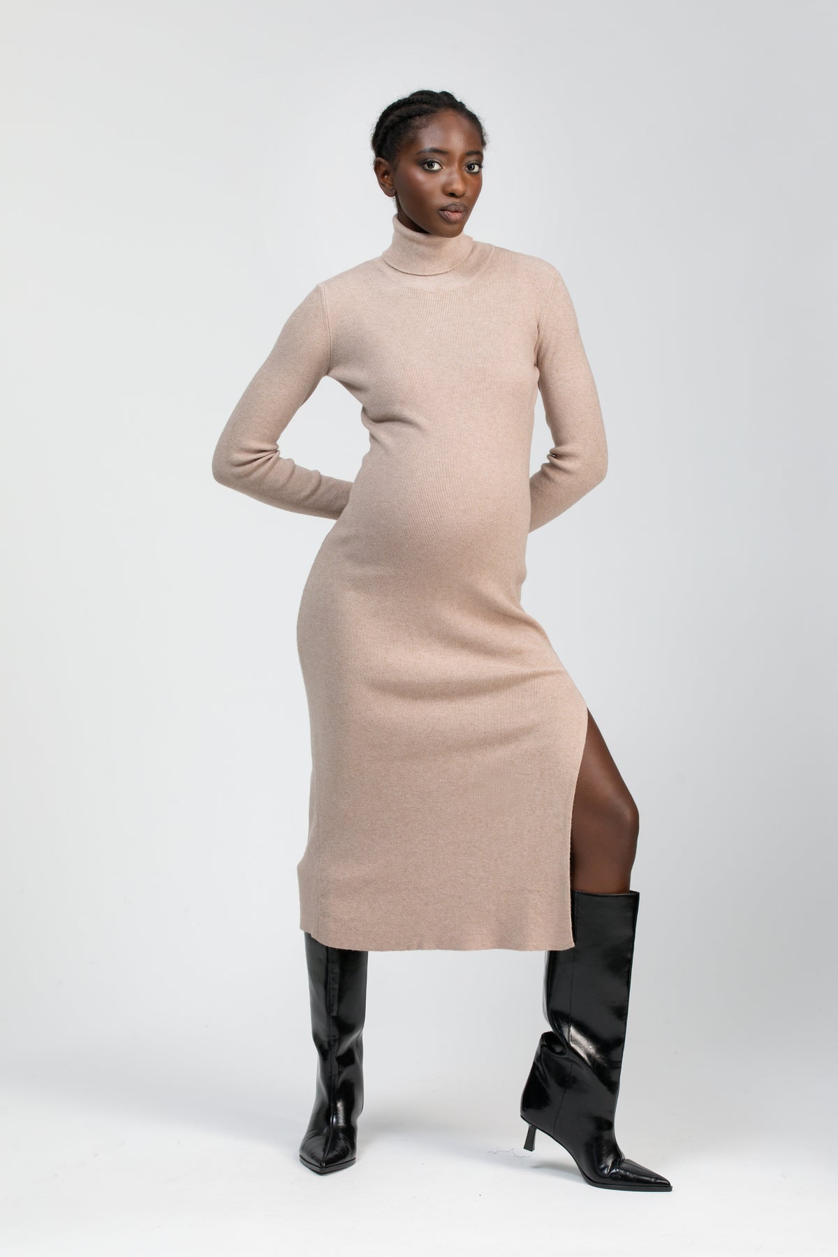 Donna incinta con abito premaman beige a collo alto e spacco laterale, stivali neri