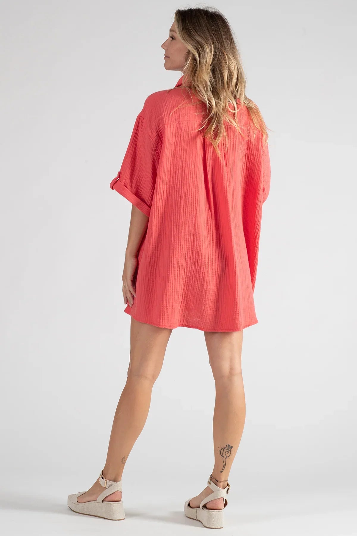 Donna di spalle con camicia premaman corallo maniche corte e sandali beige
