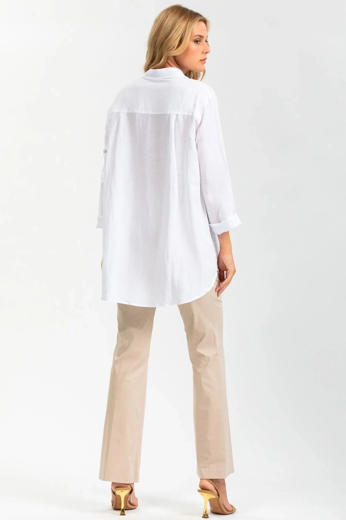 Donna con camicia premaman bianca oversize, pantaloni beige e sandali con tacco, vista posteriore