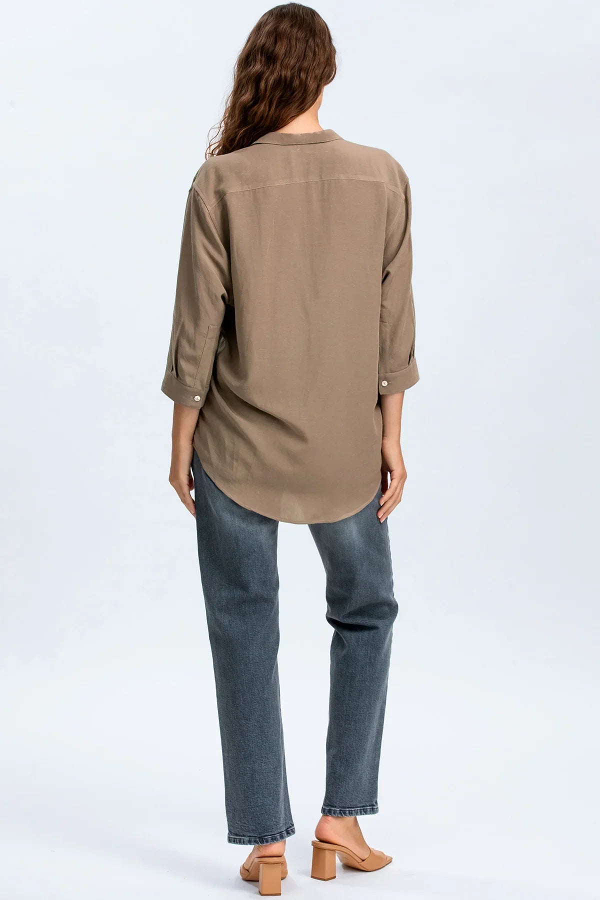Donna di spalle con camicia premaman beige e jeans dritti, look abbigliamento gravidanza