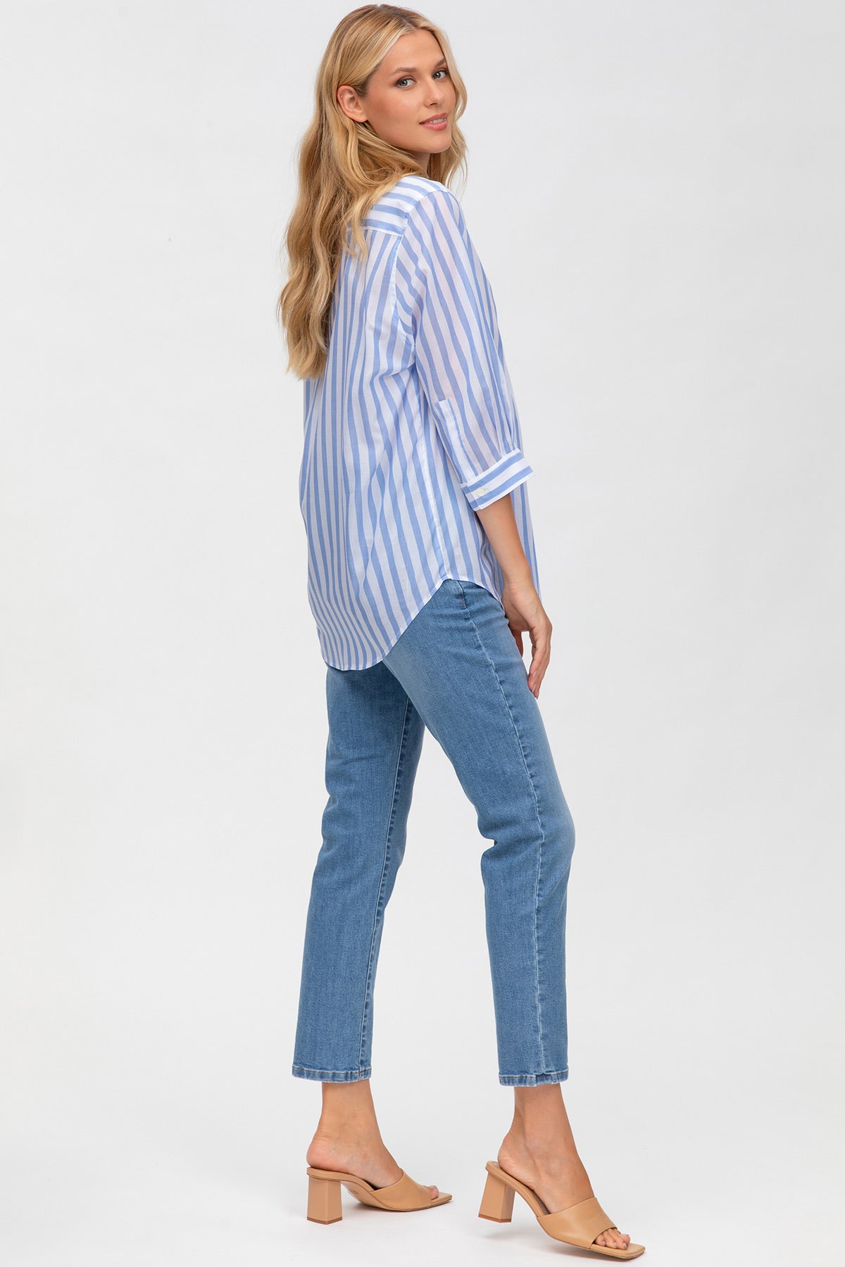 Donna incinta indossa camicia premaman a righe azzurre e pantaloni jeans, vista posteriore.