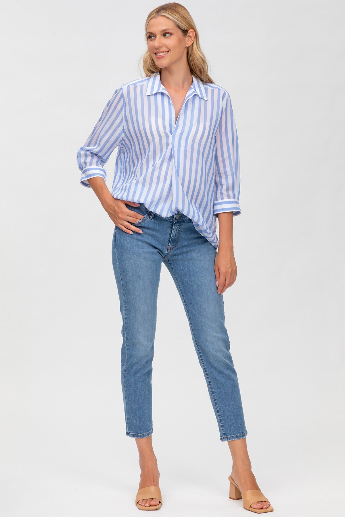 Donna con camicia premaman a righe bianche e azzurre, jeans skinny, fondo bianco.