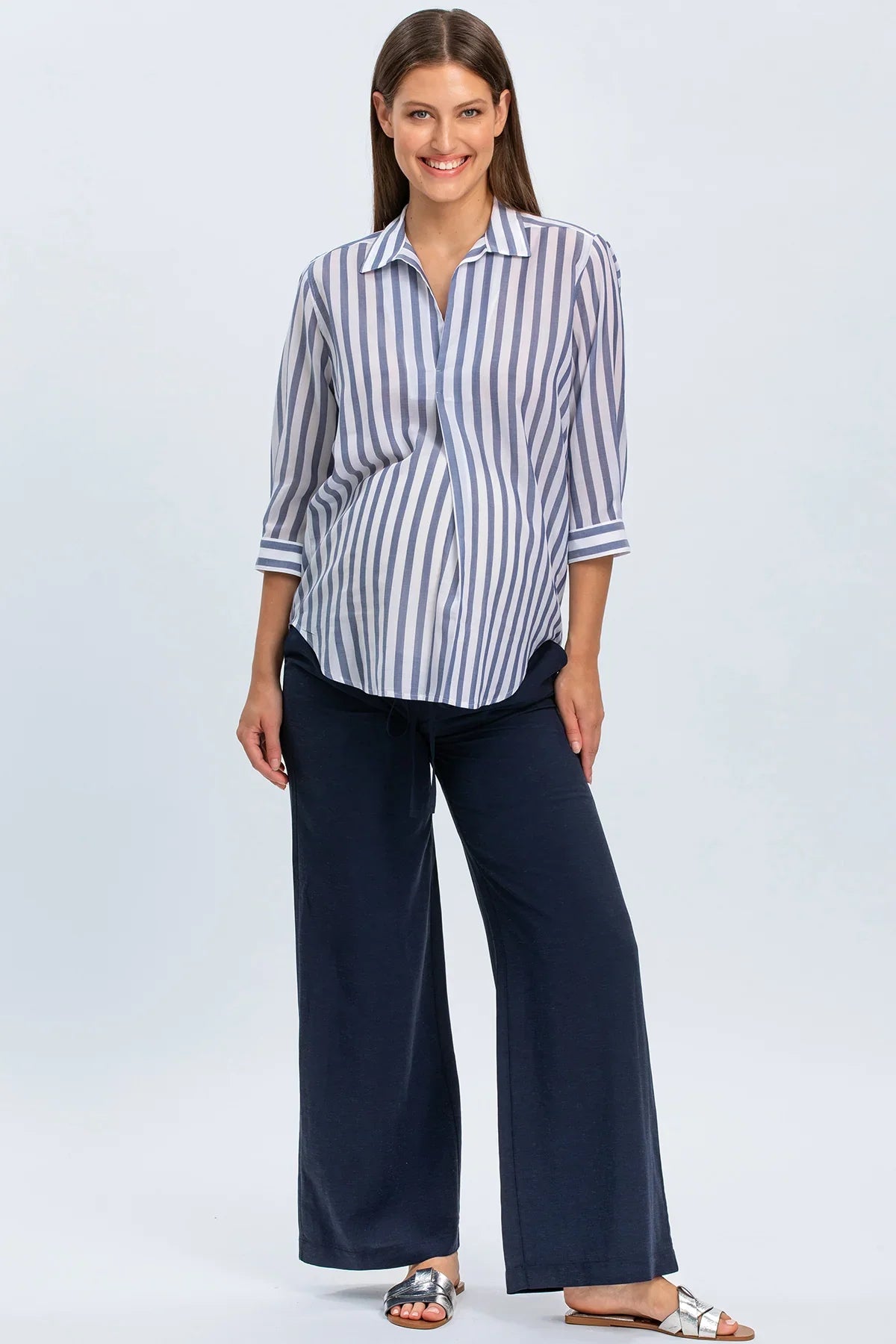 Donna incinta con camicia premaman a righe blu e pantaloni larghi navy in studio