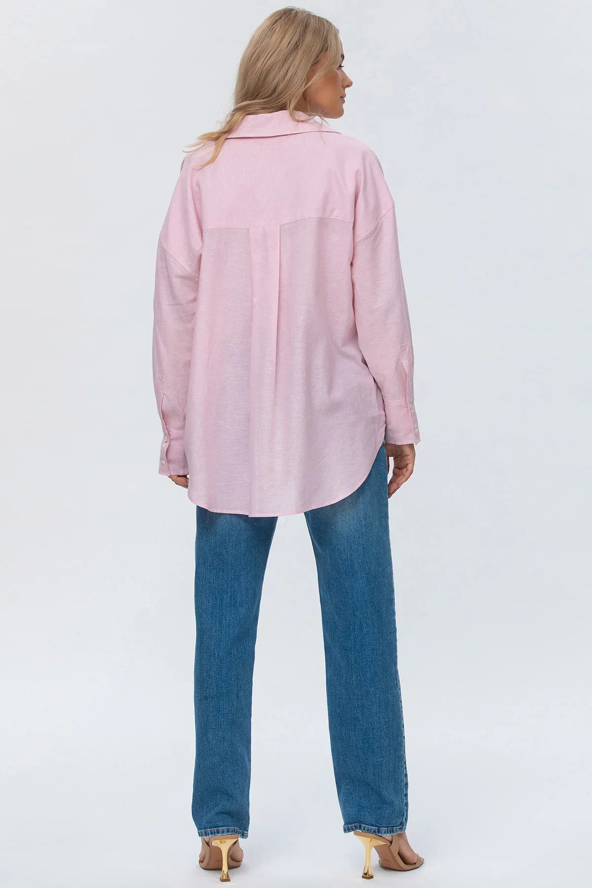 Donna di spalle con camicia rosa oversize e jeans dritti premaman, sfondo neutro.