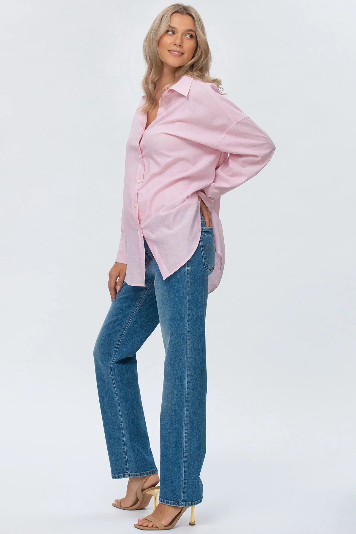 Donna incinta indossa camicia rosa e jeans premaman a vita alta dritti, stile casual elegante.