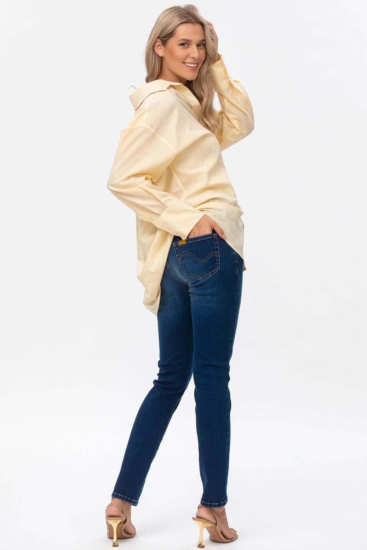 Donna sorridente con camicia premaman gialla, jeans aderenti blu e sandali tacco alto