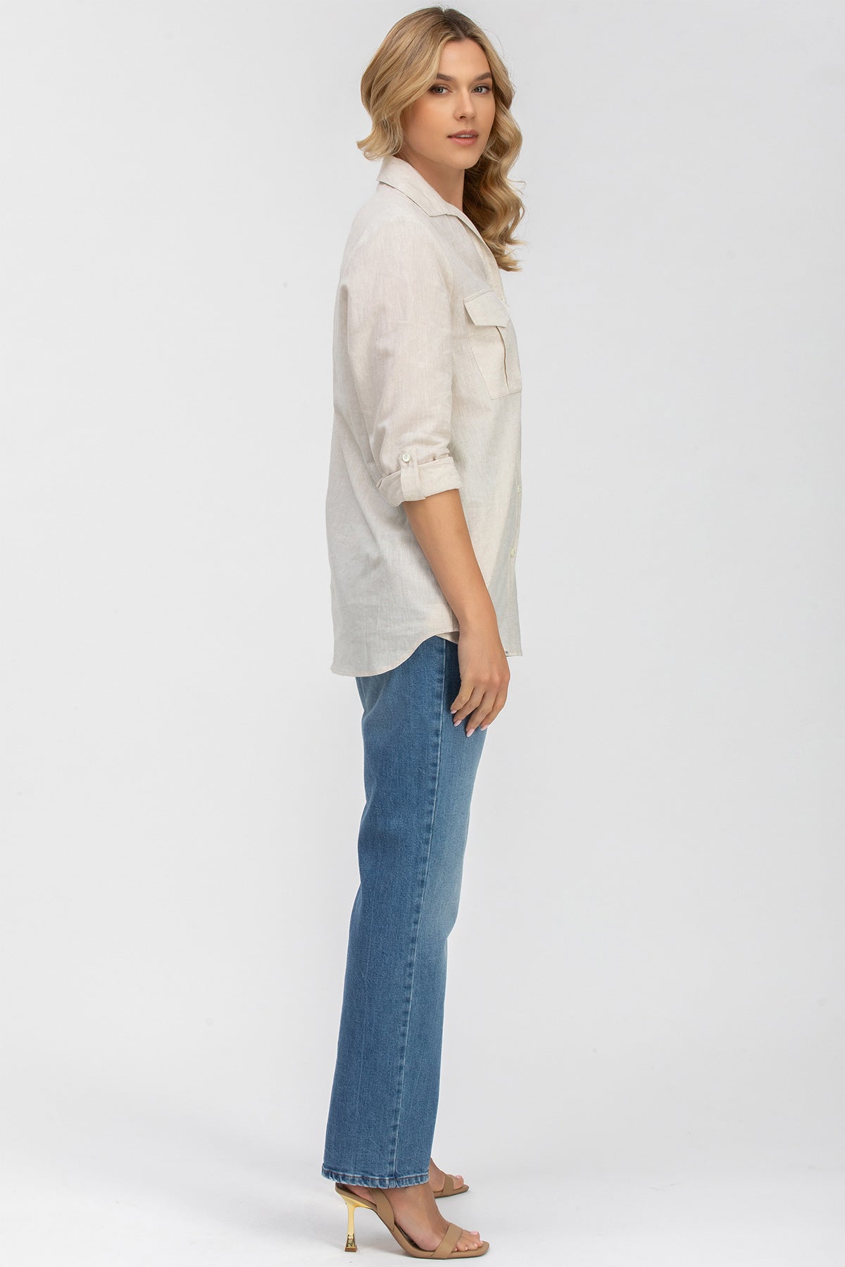 Donna incinta con camicia safari beige a maniche lunghe e jeans premaman su sfondo bianco