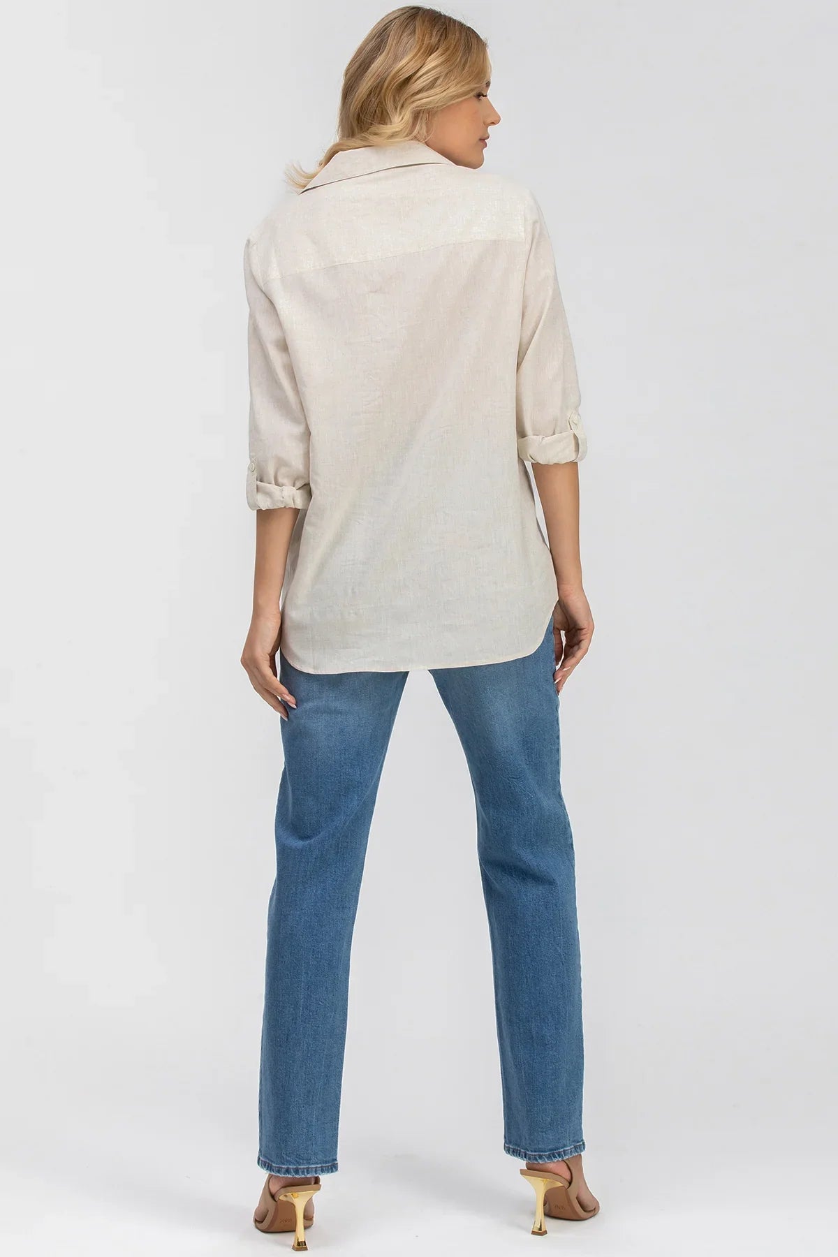 Donna di spalle con camicia lino beige maniche arrotolate e jeans premaman