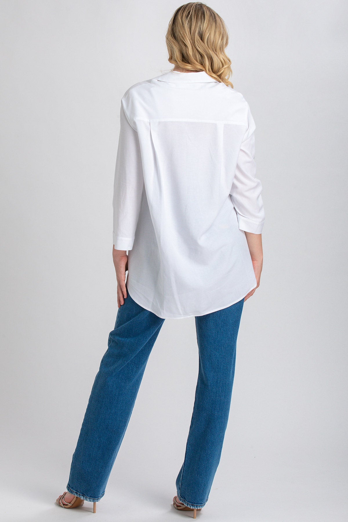 Donna di schiena indossa camicia premaman bianca e jeans dritti, fondo neutro