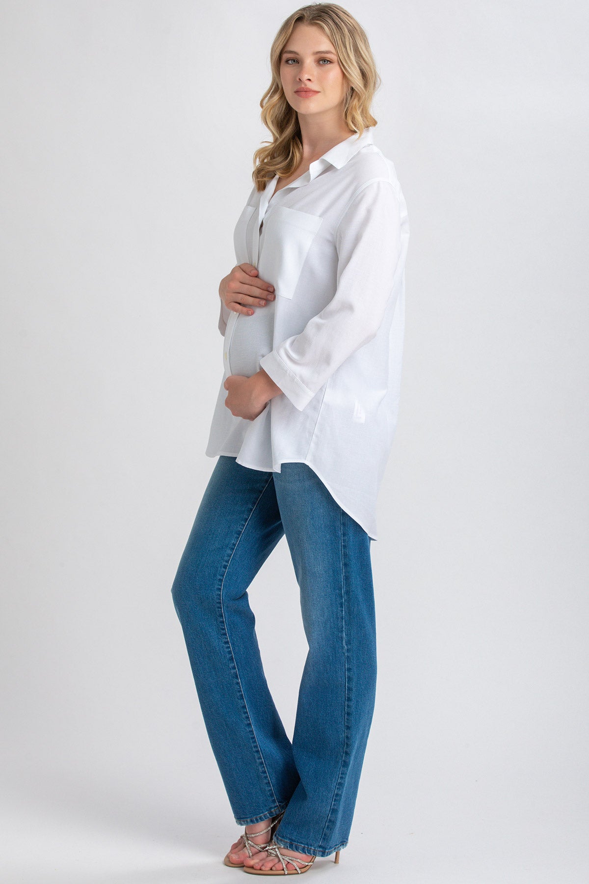 Donna incinta con camicia bianca premaman e jeans dritti in denim, sfondo neutro.