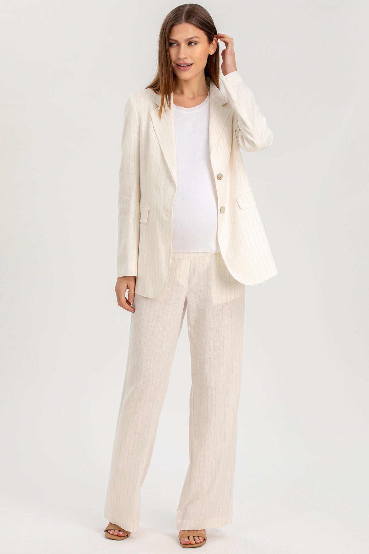 Donna incinta indossa completo premaman elegante in lino bianco, giacca e pantalone larghi.