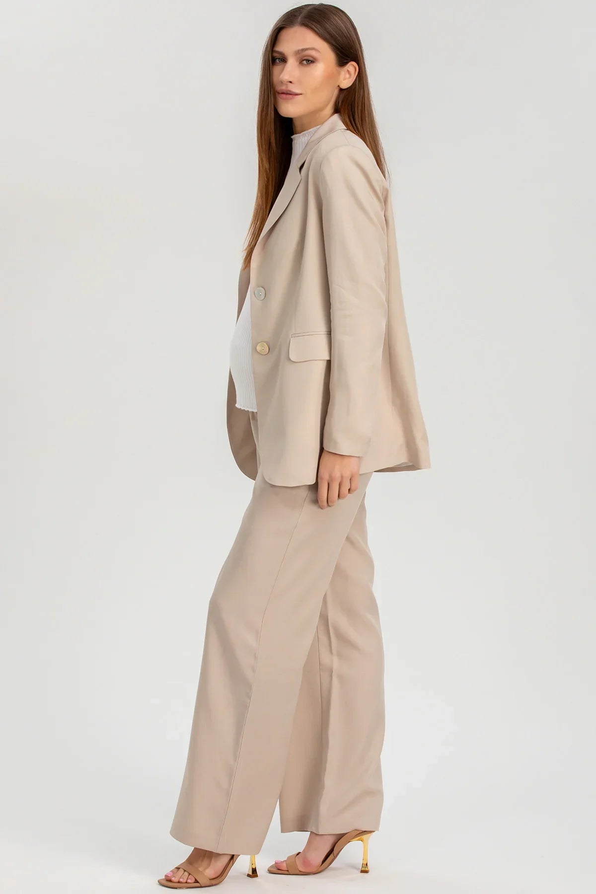 Donna premaman con completo elegante beige giacca e pantaloni, tacchi nude, sfondo neutro