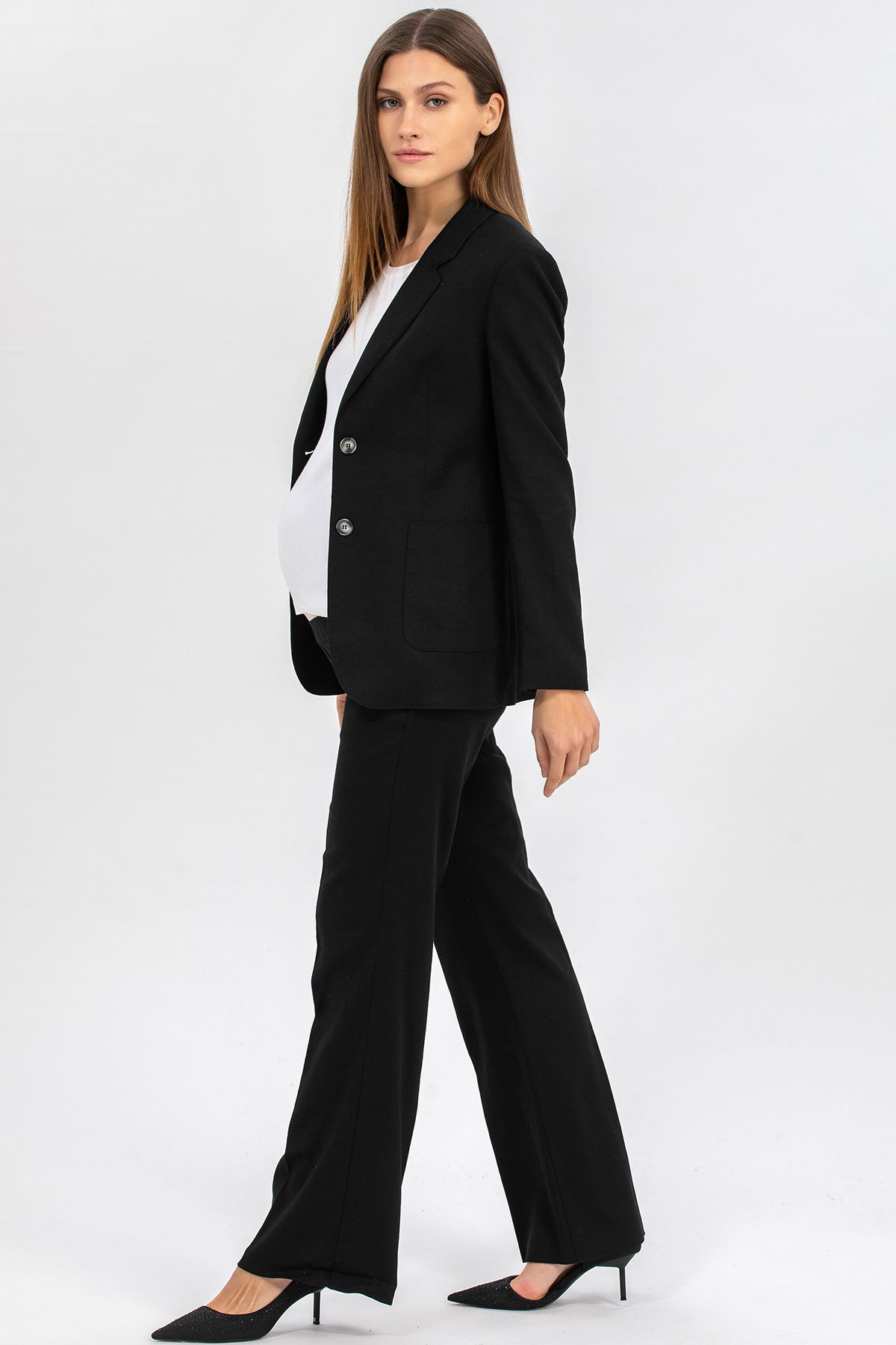 Donna incinta con tailleur premaman nero elegante e scarpe con tacco su sfondo chiaro