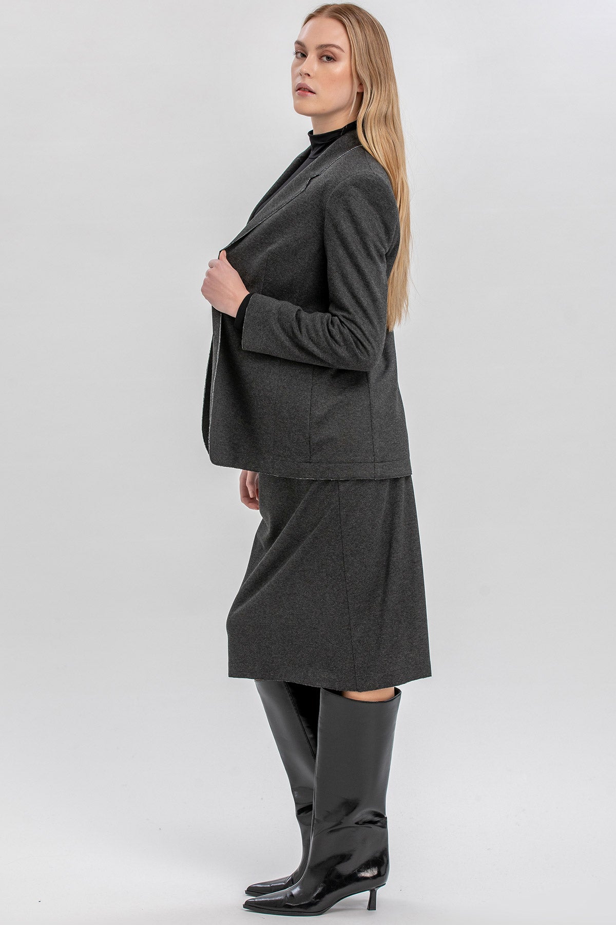 Donna in abito premaman grigio con blazer e stivali neri eleganti, su sfondo chiaro.