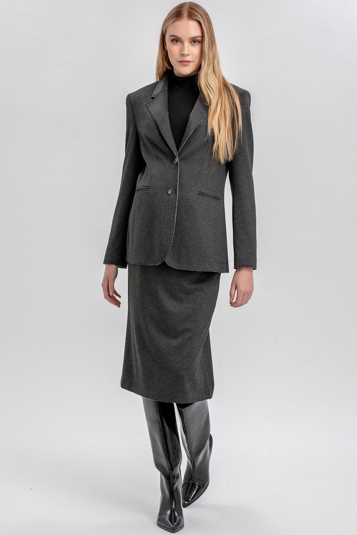 Donna in abito premaman elegante con giacca grigia, gonna midi e stivali neri