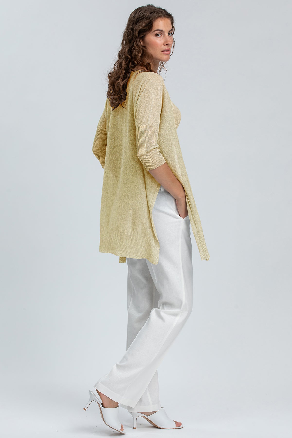 Donna indossa abbigliamento premaman elegante: maglia lunga beige e pantaloni bianchi