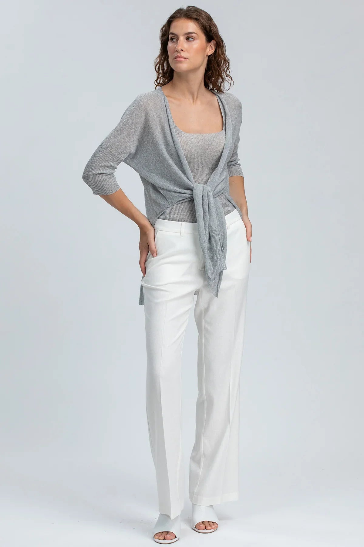 Donna indossa abbigliamento premaman elegante: maglia grigia e pantaloni bianchi larghi