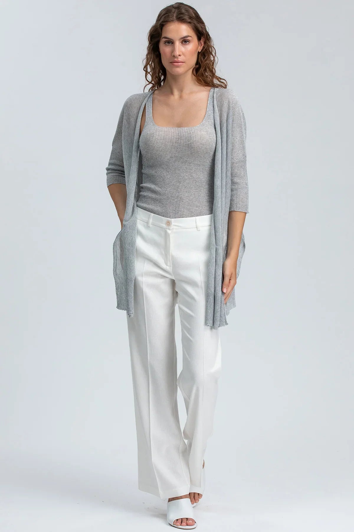 Modella indossa cardigan grigio e pantaloni bianchi premaman eleganti su sfondo neutro
