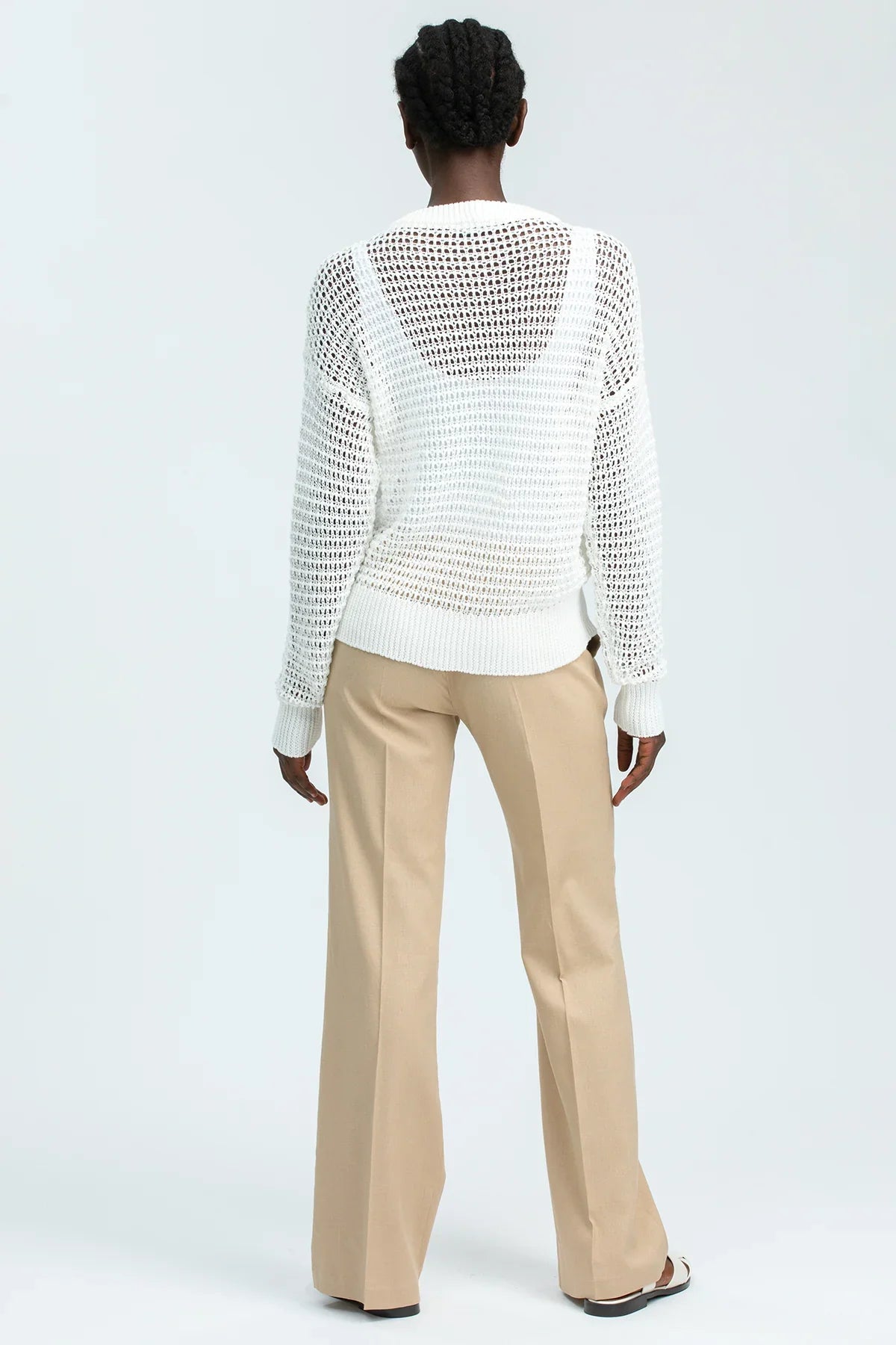 Donna di spalle con maglione premaman traforato bianco e pantaloni beige eleganti.