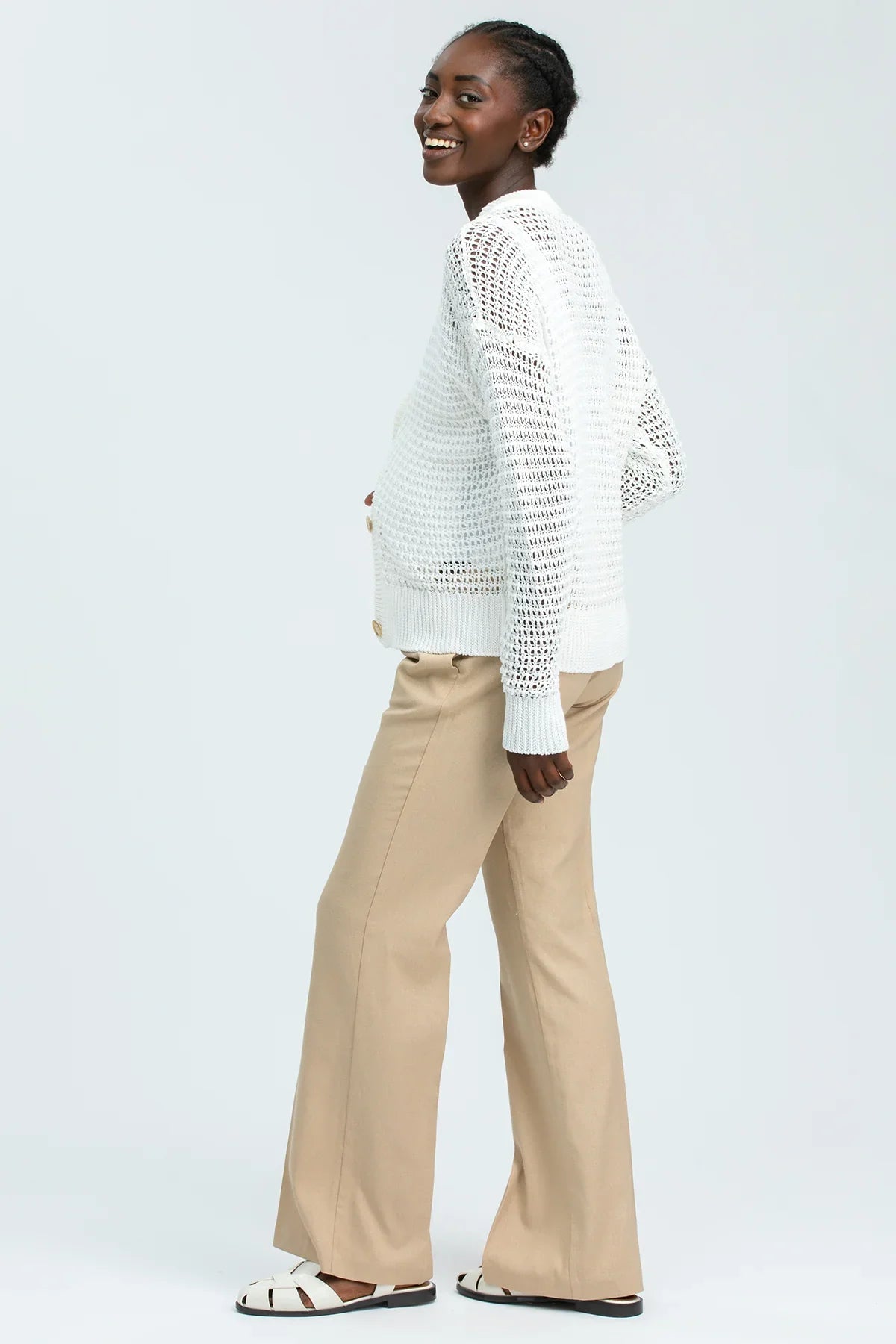 Modella indossa maglione premaman bianco traforato e pantaloni beige in stile elegante.