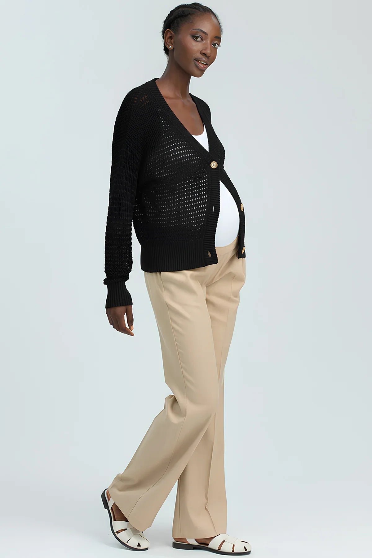 Modella incinta con cardigan premaman nero, pantaloni beige e sandali bianchi