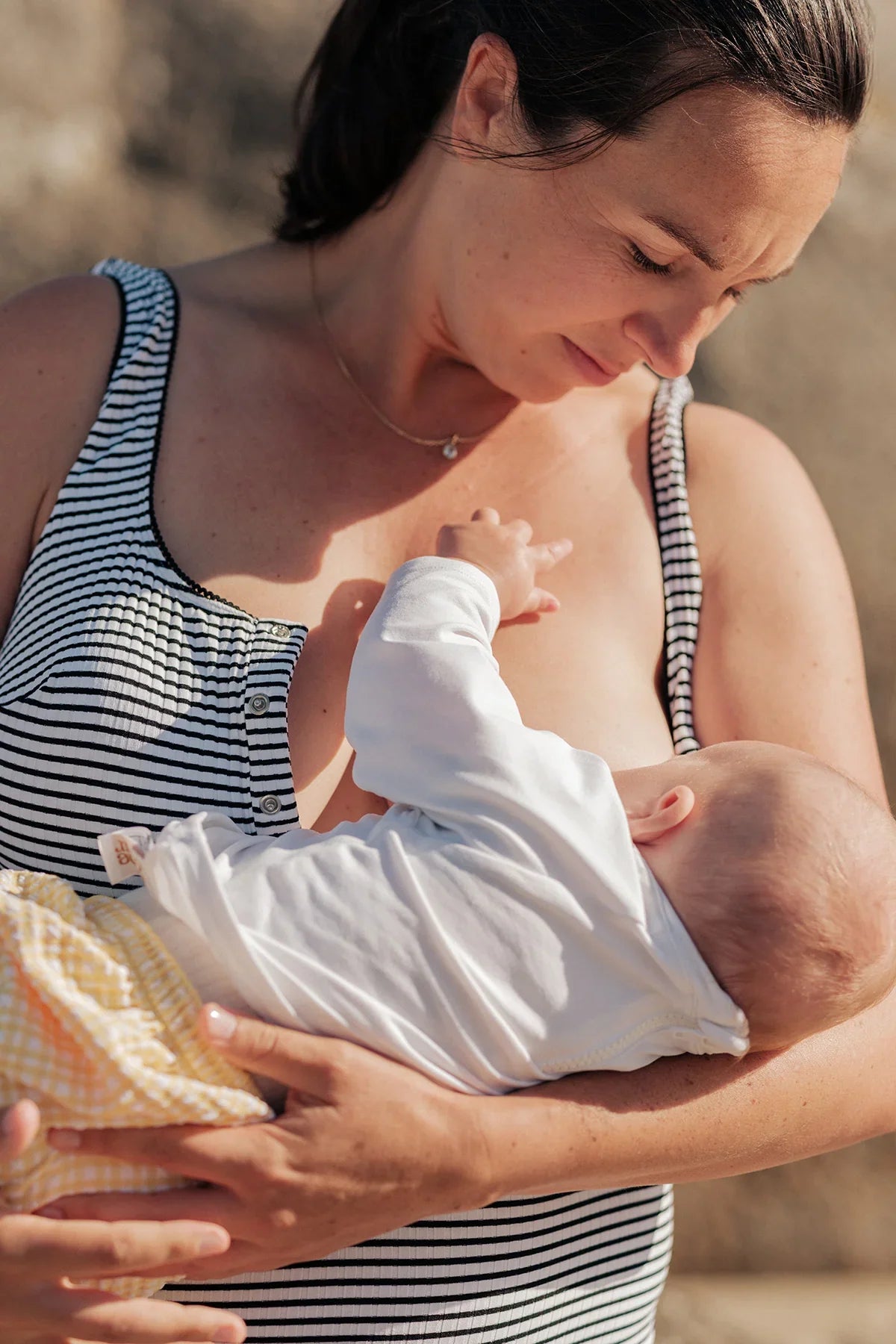 Donna con abito premaman allattamento a righe bianche e nere mentre tiene in braccio un neonato.