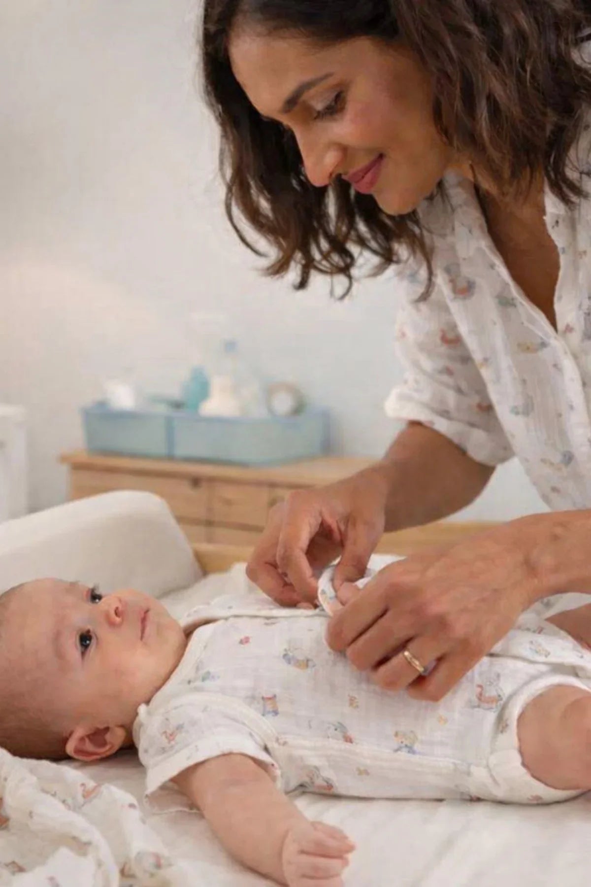 Mamma che veste un neonato su un fasciatoio, abbigliamento premaman comodo e pratico.