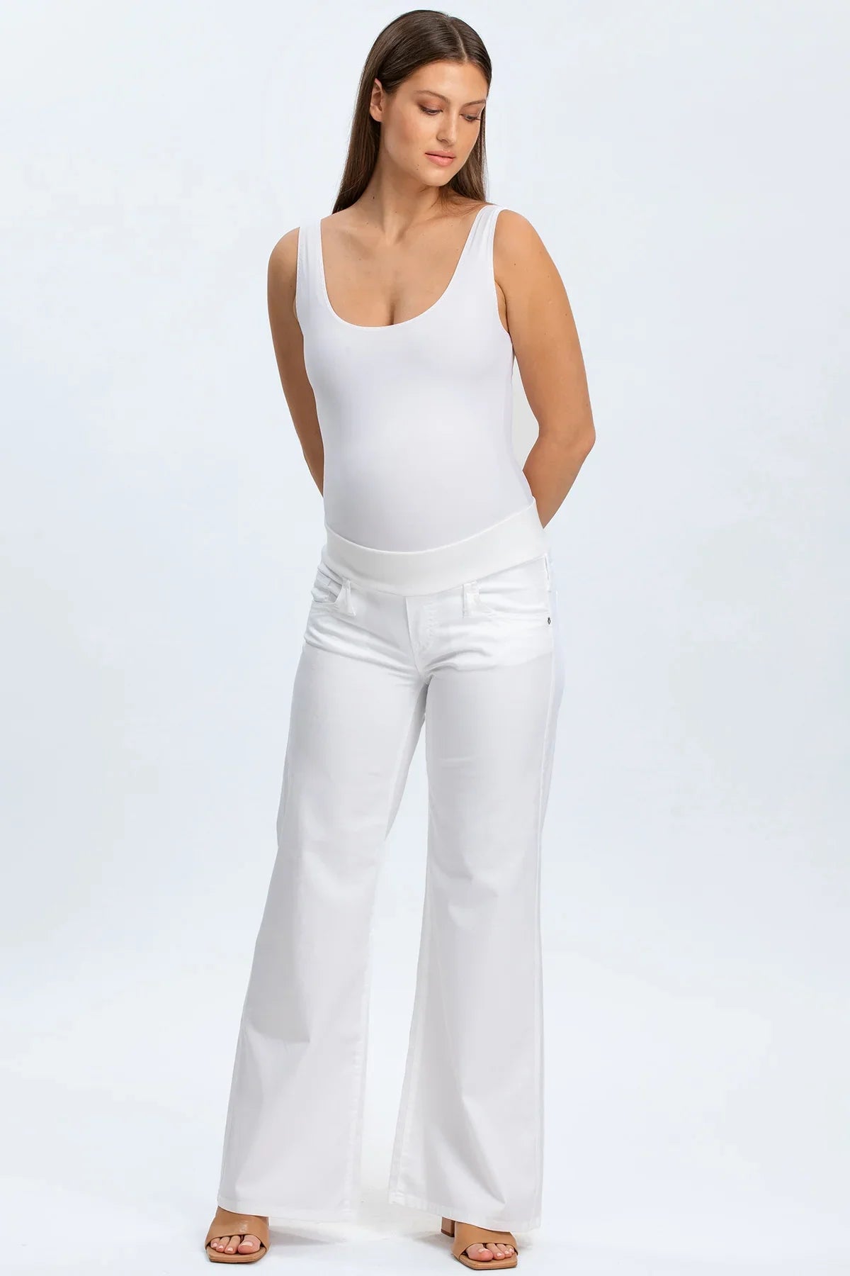 Donna che indossa pantaloni premaman bianchi a vita alta e body bianco, abbigliamento premaman elegante