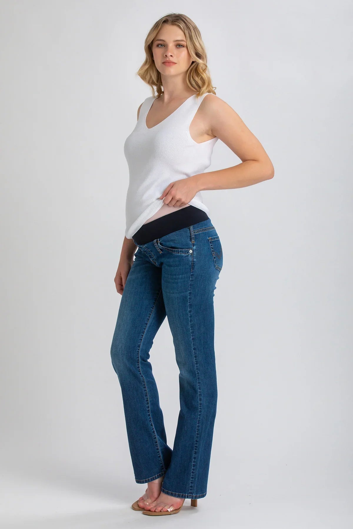 Modella con jeans premaman bootcut blu e fascia elastica, top bianco senza maniche