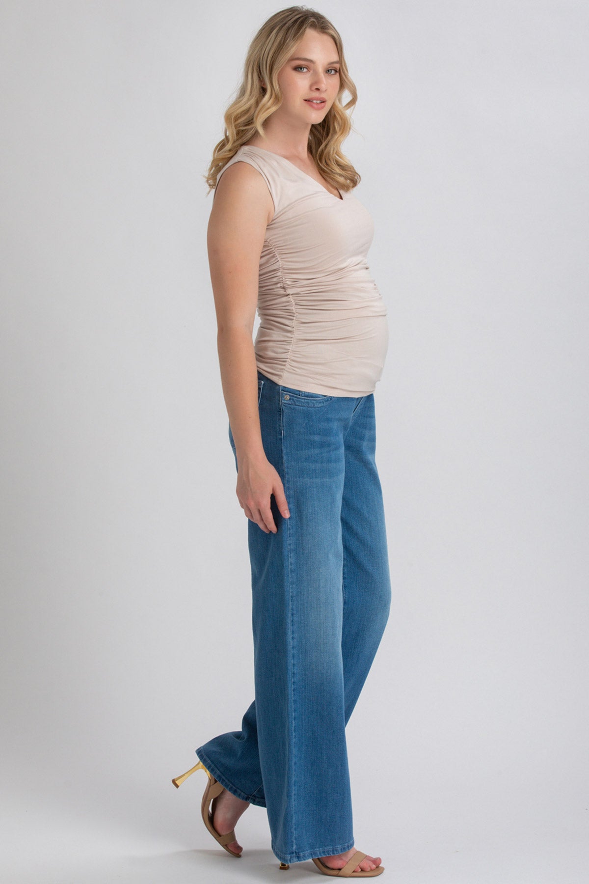 Donna incinta con top premaman beige e jeans larghi, moda abbigliamento premaman elegante